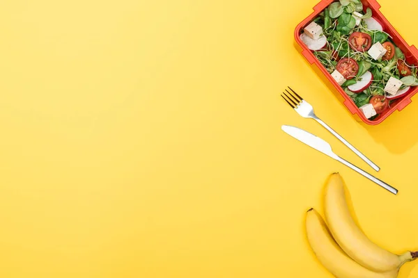 Top view of bananas, fork and knife near lunch box with salad — Stock Photo