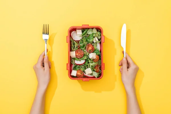 Cropped view of woman holding fork and knife over lunch box with salad — Stock Photo