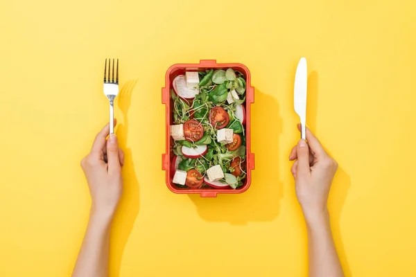 Vue recadrée de la femme tenant fourchette et couteau sur la boîte à lunch avec salade — Photo de stock