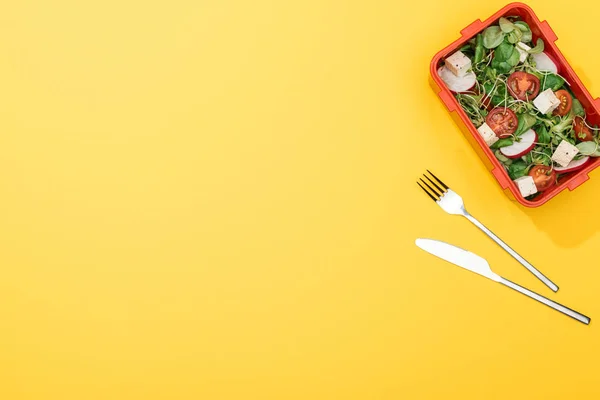 Top view of lunch box with salad near fork and knife — Stock Photo
