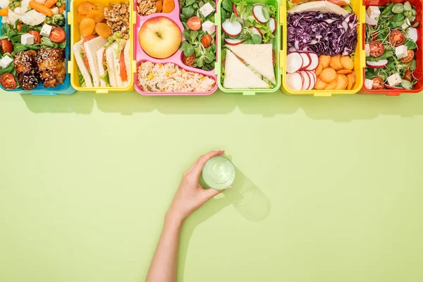 Cropped view of woman holding glass of water in hand near lunch boxes with food — Stock Photo