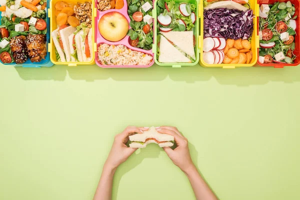 Vista recortada de la mujer sosteniendo sándwich en las manos cerca de loncheras con comida - foto de stock
