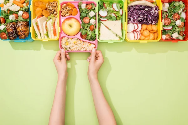 Vista cortada da mulher escolhendo lancheiras com comida no fundo verde — Fotografia de Stock