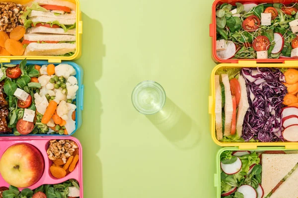 Vista superior de loncheras con comida cerca de vaso de agua - foto de stock