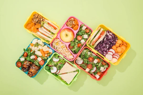 Disposición plana de loncheras con comida sobre fondo verde - foto de stock