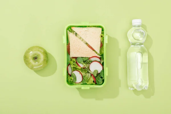 Draufsicht auf Lunchbox mit Salat und Sandwiches in der Nähe der Flasche mit Wasser und grünem Apfel — Stockfoto