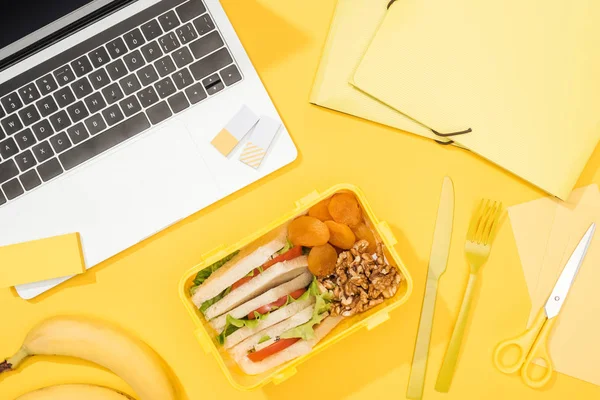 Vue du dessus de la boîte à lunch avec de la nourriture près d'un ordinateur portable et des fournitures de bureau — Photo de stock