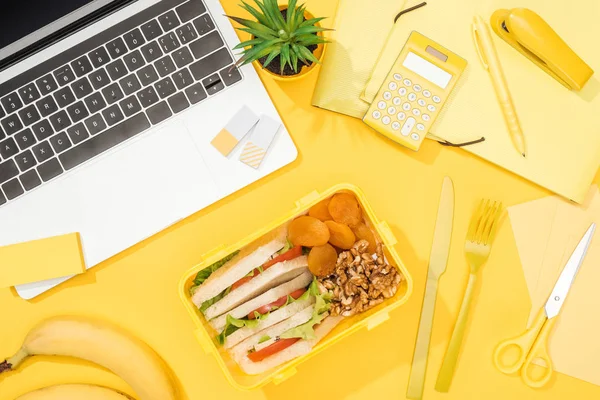 Top view of lunch box with food near laptop and office supplies — Stock Photo