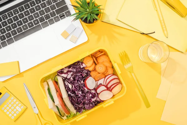 Blick von oben auf leckeres Mittagessen in Schachtel am Arbeitsplatz mit gelbem Hintergrund — Stockfoto