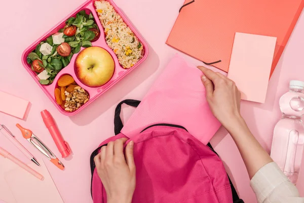 Cropped view of woman packing backpack near lunch box with food and stationery — Stock Photo