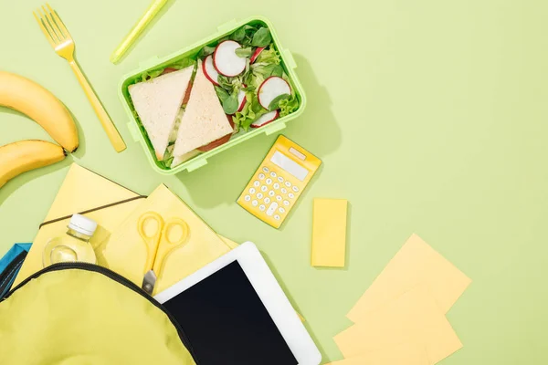 Вид на обеденную коробку с бутербродами и салатом рядом с рюкзаком с канцелярскими принадлежностями — стоковое фото