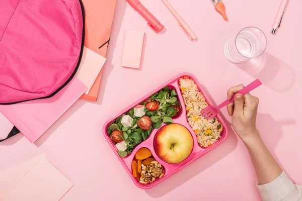 Vista ritagliata delle mani della donna con utensili di plastica sopra la scatola di pranzo con cibo vicino allo zaino e alla cancelleria — Foto stock