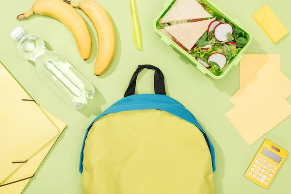 Top view of lunch box with food near backpack, bottle of water and stationery — Stock Photo