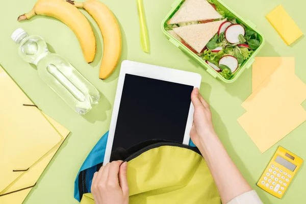 Cropped view of woman packing digital tablet in backpack near lunch box, bananas, bottle of water and stationery — Stock Photo