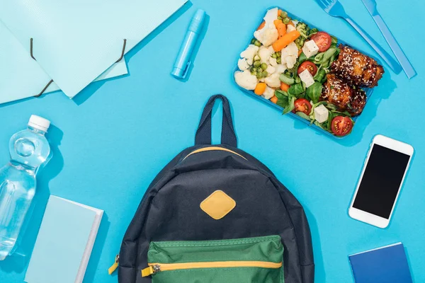 Vue du dessus du sac à dos près de la boîte à lunch, papeterie, smartphone et bouteille d'eau — Photo de stock