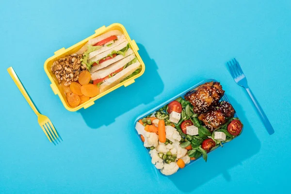 Top view of plastic forks near lunch boxes with food on blue background — Stock Photo