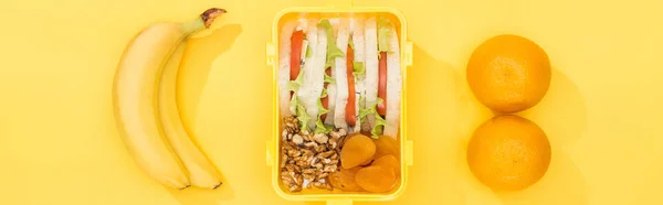 Panoramic shot of lunch box with food near bananas and oranges — Stock Photo