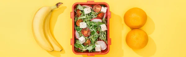 Panoramic shot of lunch box with food near bananas and oranges — Stock Photo