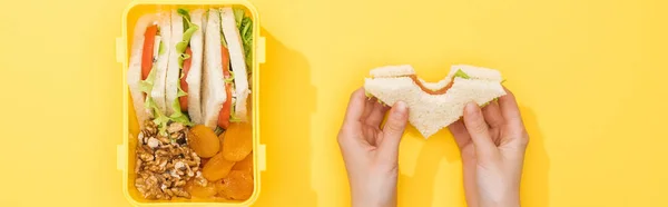 Cropped view of woman holding sandwich in hands near lunch box with food — Stock Photo