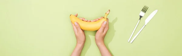 Vista cortada da mulher segurando banana nas mãos perto de garfo e faca — Fotografia de Stock