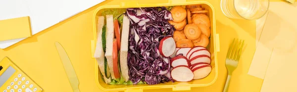 Panoramic shot of lunch box with food near banana, knife and fork — Stock Photo