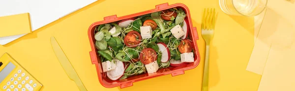 Panoramic shot of lunch box with salad near banana, knife and fork — Stock Photo