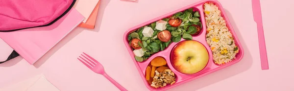 Panoramic shot of lunch box with food near fork, backpack and stationery — Stock Photo