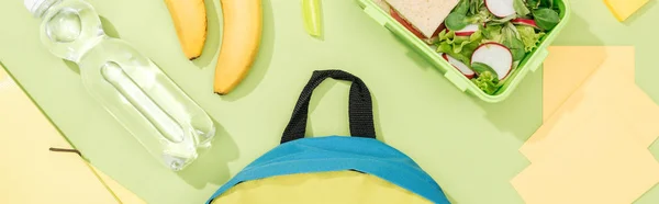 Panoramaaufnahme von Rucksack in der Nähe von Flasche mit Wasser, Lunchbox, Bananen und Schreibwaren — Stockfoto