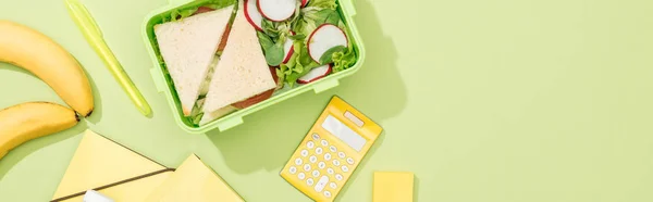 Panoramic shot of lunch box with food near office supplies — Stock Photo
