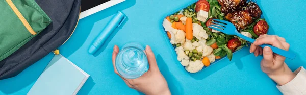 Cropped view of woman with lunch box and glass of water near backpack — Stock Photo