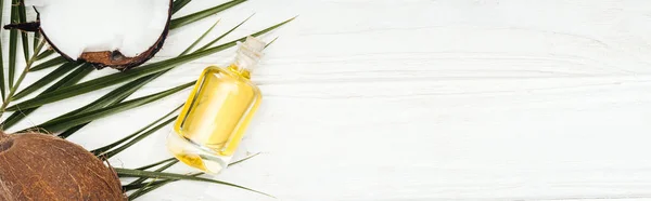 Top view of coconut oil in bottle on green palm leaf on white wooden surface, panoramic shot — Stock Photo