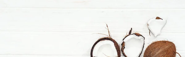 Vue de dessus des moitiés de noix de coco sur la surface en bois blanc, vue panoramique — Photo de stock