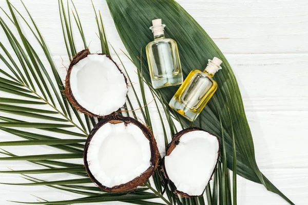 Vue du dessus de l'huile de coco en bouteilles sur des feuilles de palme vertes sur une surface en bois blanc — Photo de stock