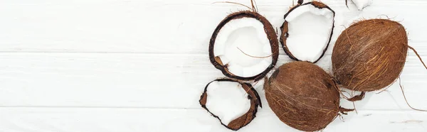 Top view of cracked and whole coconuts on white wooden surface, panoramic shot — Stock Photo