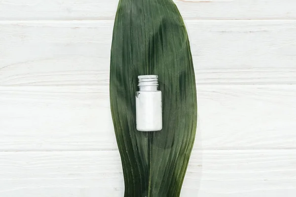 Вид сверху на кокосовую косметику в бутылке на зеленом пальмовом листе на белой деревянной поверхности — стоковое фото