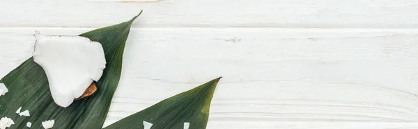 Vue du dessus des morceaux de noix de coco sur des feuilles de palmier vert sur une surface en bois blanc avec espace de copie, vue panoramique — Photo de stock