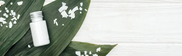 Vista superior del producto de belleza de coco en botella en hojas de palma verde con hojuelas de coco en superficie de madera blanca con espacio de copia, plano panorámico - foto de stock