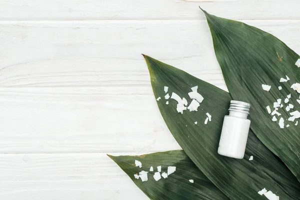 Vue du dessus du produit de beauté de noix de coco en bouteille sur des feuilles de palmier vertes avec des flocons de noix de coco sur une surface en bois blanc — Photo de stock