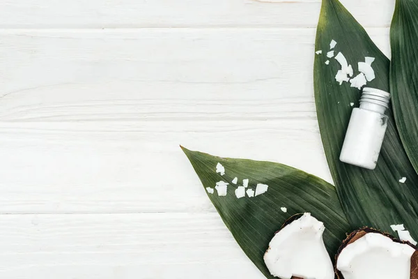 Top view of coconut beauty product in bottle on palm leaves with coconut flakes on white wooden surface with copy space — Stock Photo