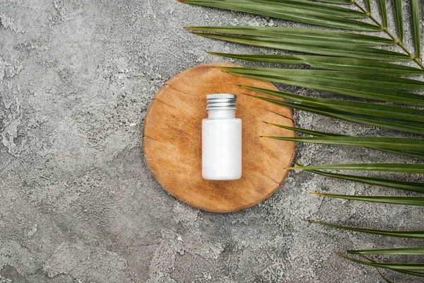 Vue du dessus du produit de beauté de noix de coco en bouteille sur une planche de bois près de la feuille de palme sur fond texturé gris — Photo de stock