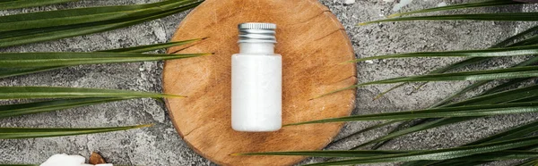 Top view of coconut beauty product in bottle on wooden board near palm leaves, panoramic shot — Stock Photo