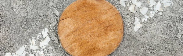 Vue de dessus des copeaux de noix de coco près de la planche de bois sur fond gris texturé, vue panoramique — Photo de stock