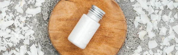 Vue du dessus des copeaux de noix de coco près du panneau en bois avec crème de noix de coco sur fond gris texturé, vue panoramique — Photo de stock