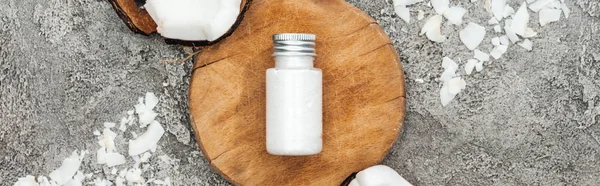 Vue du dessus des copeaux de noix de coco près du panneau en bois avec crème de noix de coco sur fond gris texturé, vue panoramique — Photo de stock