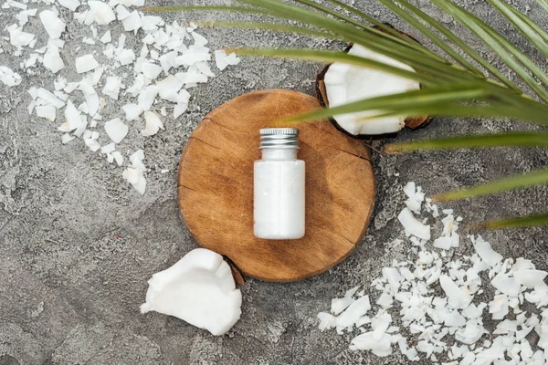 Vue du dessus des copeaux de noix de coco et de la feuille de palme près du panneau en bois avec crème de noix de coco sur fond texturé gris — Photo de stock