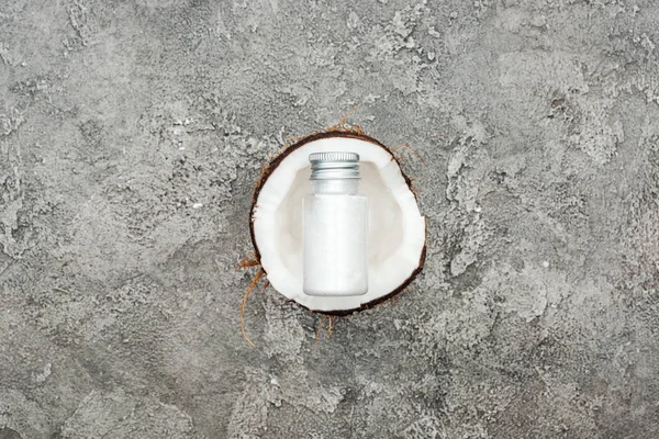 Top view of cream in bottle on coconut half on grey textured background — Stock Photo