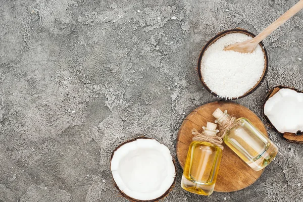 Top view of coconut oil in bottles on wooden board on grey textured background with copy space — Stock Photo