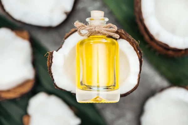 Selektiver Fokus von Kokosöl in der Flasche auf der Hälfte der weißen Kokosnuss — Stockfoto