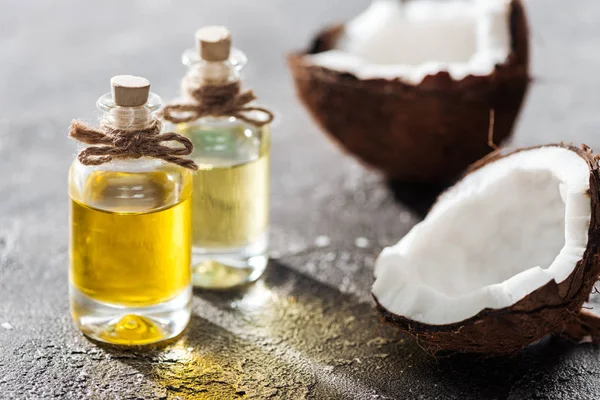 Selective focus of bottles with coconut oil near coconut halves on grey background — Stock Photo