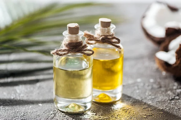 Foco seletivo de garrafas com óleo de coco perto de folha de palma verde e coco rachado — Fotografia de Stock